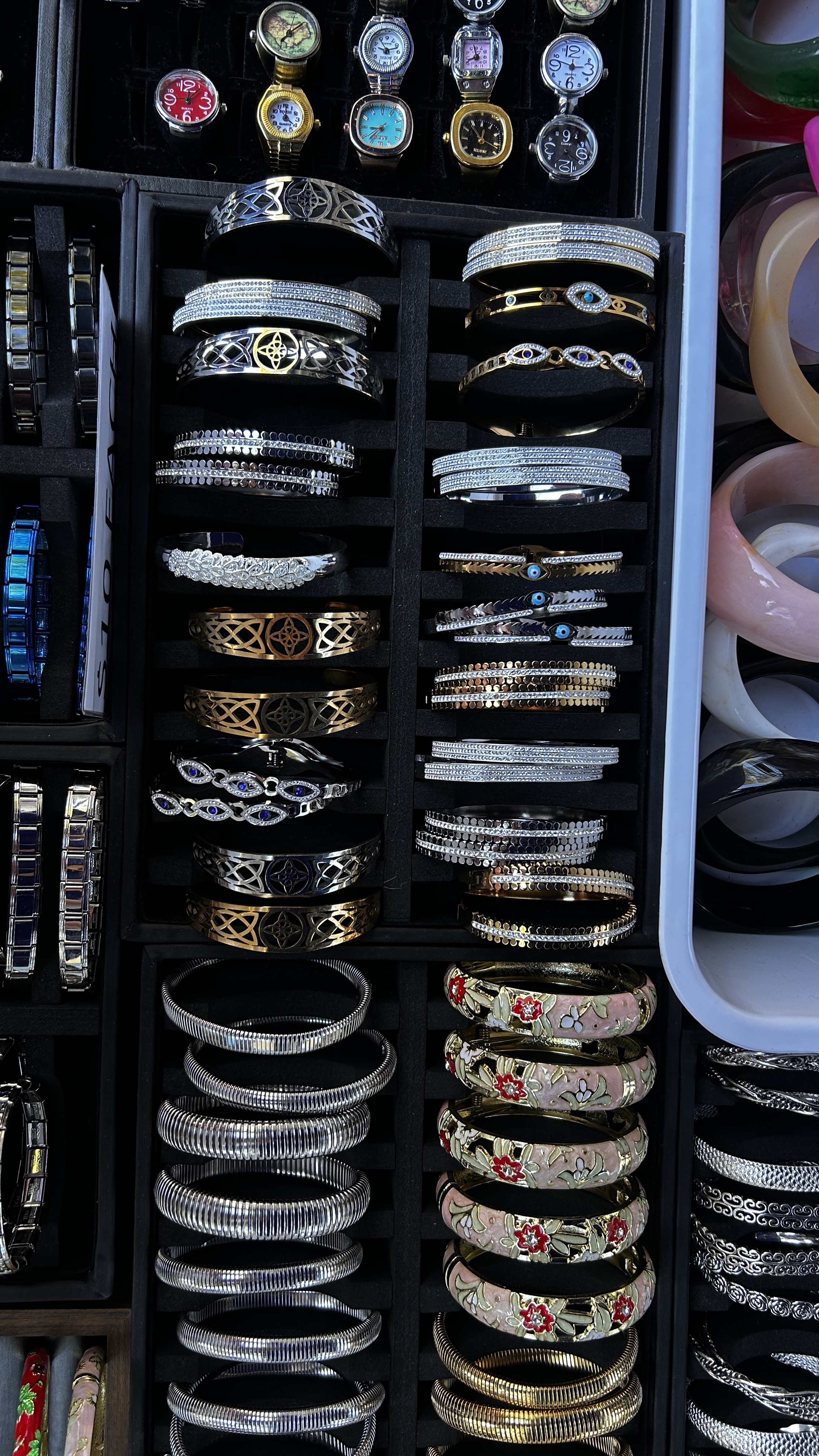 Mixed gold and silver-tone cuff bracelets in a market display.